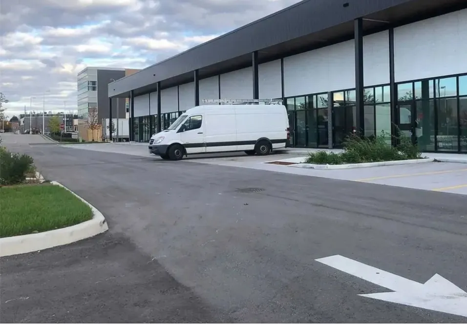 Photo of a row of storefronts along a driveway, with a parked van.