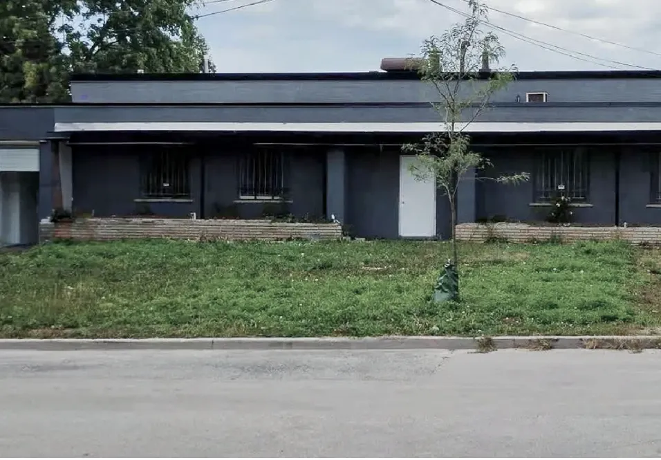 Photo of a dark single-storey building with a white door behind a lawn.